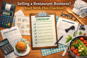 A detailed flat lay illustration of items related to selling a restaurant business. At the center is a clipboard with a green checklist. Surrounding it are documents labeled “Business Tax Returns” and “Lease Agreement,” a POS terminal, calculator, money, a burger, a pot of fresh vegetables, restaurant layout plans, cooking utensils, a chef’s hat, keys, and glasses. The background is a warm wooden table with a blue checkered napkin. Bold text at the top reads “Selling a Restaurant Business? Start With This Checklist.”