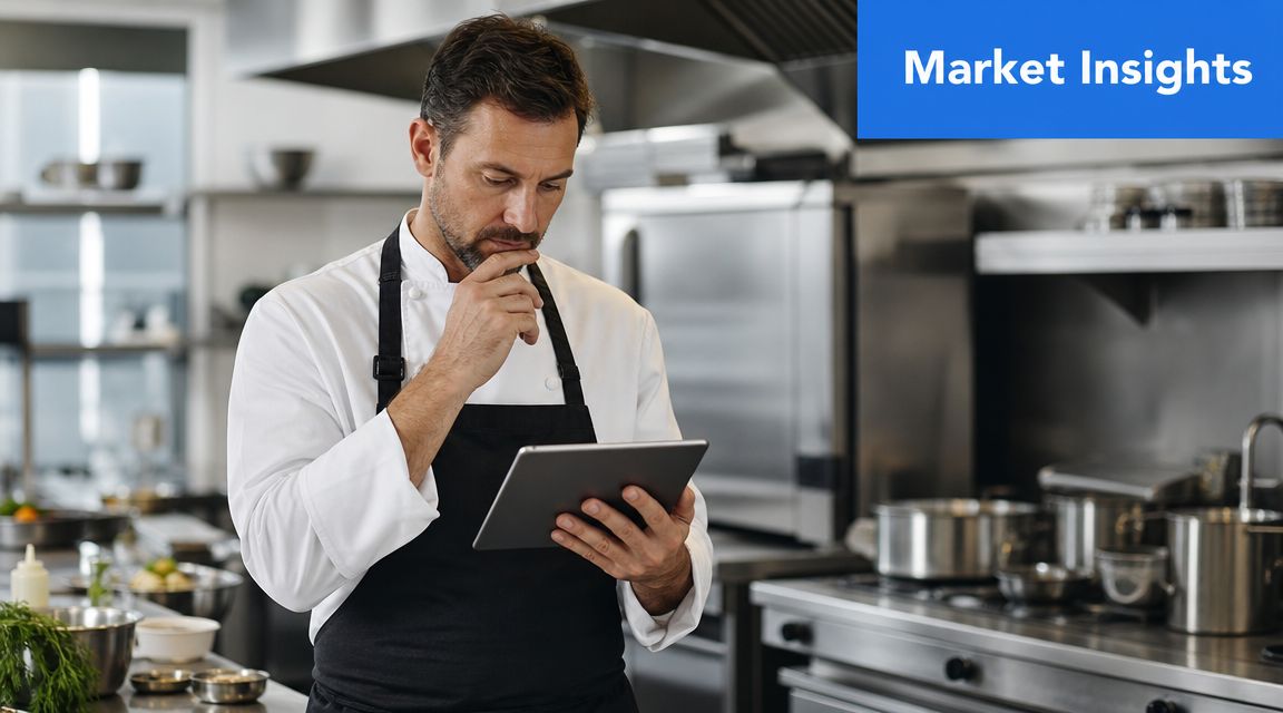 A professional male chef standing in a commercial kitchen using a tablet to review data.