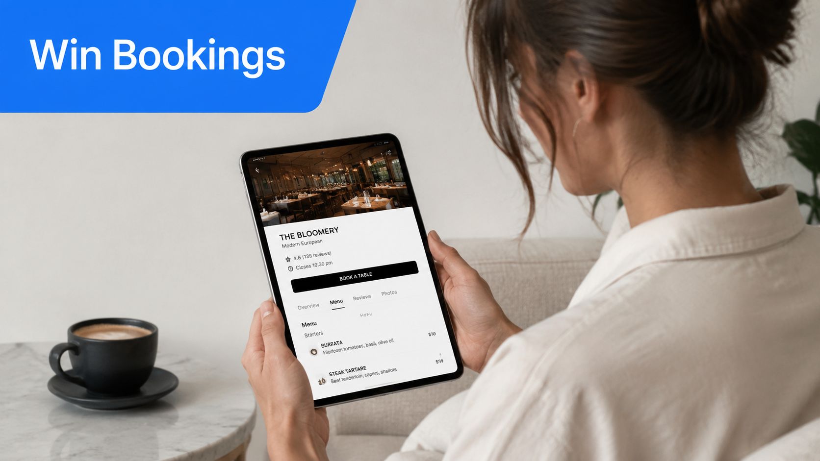 A woman holding a digital tablet displaying a restaurant booking page while sitting with a coffee.